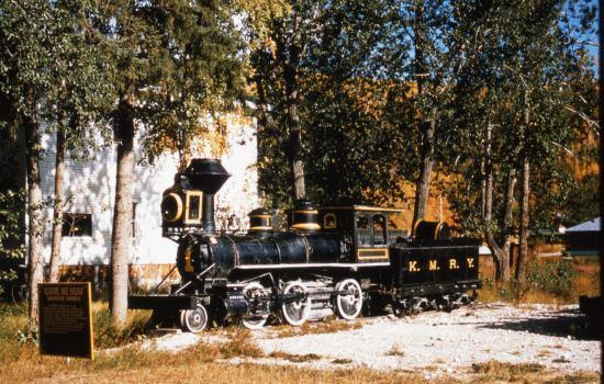 Colour view of a steam engine (Klondike Mines Railway Engine No. 1 currently in the collection of the Dawson City Museum) beside the Administration Building, now the Dawson City Museum.
